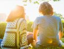 A young man and woman sit on the grass, their backs to the camera