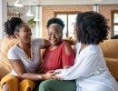 Three generations of women hug on a couch.