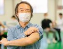 A man in a face mask rolls up his sleeve.