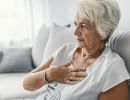  A woman sits on a couch with a hand pressed to her chest