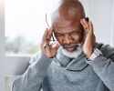 An older adult putting his fingers to his head and grimacing.