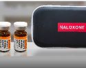 Two naloxone vials next to a small protective case labeled “NALOXONE”