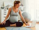A pregnant woman sits on the floor and looks at a laptop.