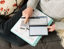 A view of someone's lap from above with a checkbook, calculator and notebook.