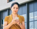 A woman with a worried expression checks her phone.