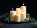 Five lighted candles of different heights on a plate with holly, pine sprigs and pine cones.