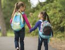 Two girls with backpacks holding hands as they walk down the street.