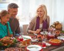 A happy man, woman, girl and boy sit at a table laden with Thanksgiving food.