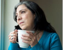 A woman holding a mug looks out a window