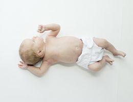 A baby in a cloth diaper lies on a flat mattress.