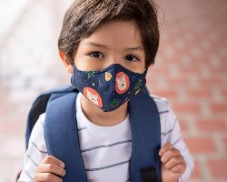 A young boy wearing a patterned mask and a backpack.