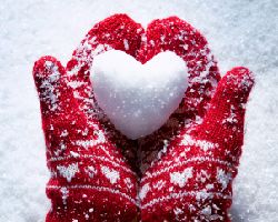 Hands with mittens holding a heart shaped snowball.