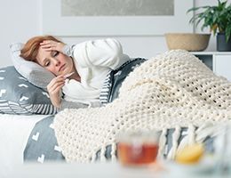 A woman lies in bed looking at a thermometer.