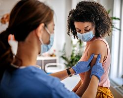 A woman in scrubs bandages another woman’s arm after a vaccine.
