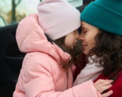 A woman rubs noses with a young girl next to an open car door.