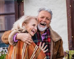 Two warmly-dressed seniors laugh outdoors.