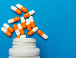 Orange and white capsules spill out of a white bottle onto a blue background