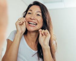 A smiling woman flosses her teeth.