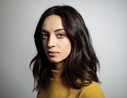 A young woman in a yellow sweater looks at the camera.