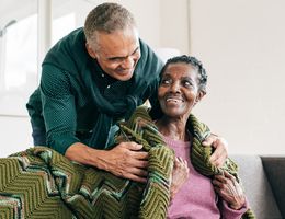 A man tucks a blanket over an older woman’s shoulders