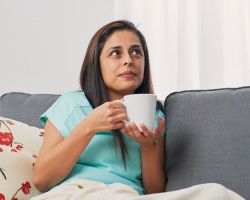 A woman sits on a couch holding a mug.
