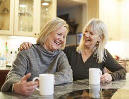 Two women sit laughing. One has her arm around the other’s shoulders.