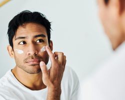 A man stripes his cheeks with sunscreen while looking in a mirror.