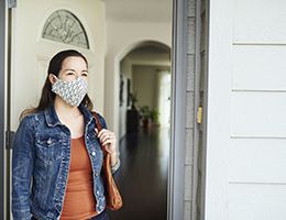 A woman in a face mask walks out her front door.