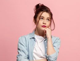 A young woman rests her chin on one hand, thinking.