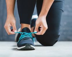 Hands tighten the blue laces of a running shoe.