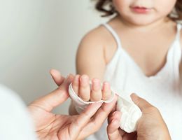 A young child having their hand wrapped in a bandage.