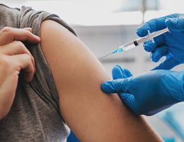 Gloved hands inserting a syringe into someone's upper arm.