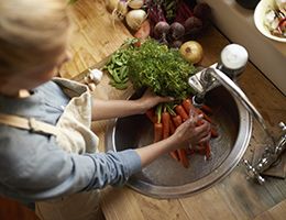 A woman washes a bunch of carrots in a sink.