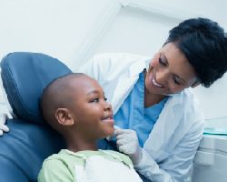 A boy smiles as he leans back in an exam chair. His dentist smiles back.