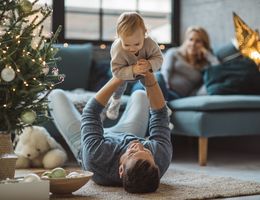 A man lies on the floor and holds a toddler in the air