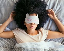 A woman lies in bed with a sleep mask over her eyes.