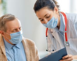 A masked doctor shows her tablet to a masked patient.