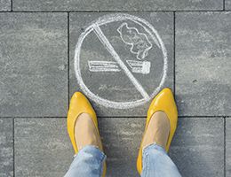 A woman is standing next to a no smoking symbol drawn on a sidewalk.