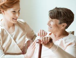 A young woman smiles at a seated older woman who is holding a cane