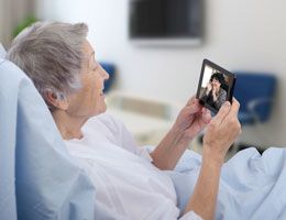 A woman in a hospital bed video chats on a smartphone.