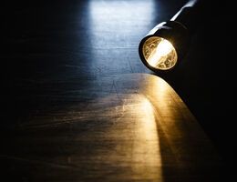 A lighted flashlight on a hardwood floor.