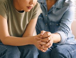 Clasped hands of a young woman and an older woman who are sitting next to each other.