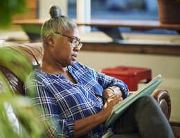 A woman sits on a couch taking notes on a pad of paper.