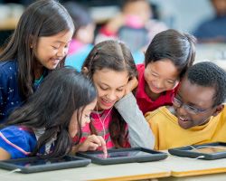 A group of kids gather around a book, their heads close together.