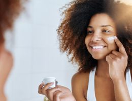 A young woman looking in a mirror puts skin cream on her cheek.