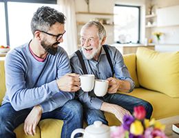 A father and son sitting on a couch drinking coffee.