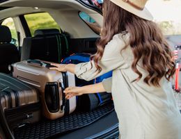 A woman loads suitcases into the back of a car.