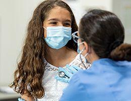 A child wearing a mask is having her heart listened to by a nurse who is also wearing a mask.