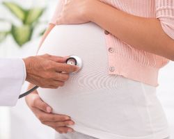 Hands hold a stethoscope to the stomach of a pregnant woman.