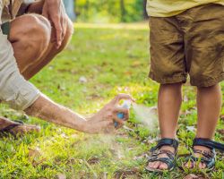 An adult squats to spray mosquito repellent on a child’s ankles.